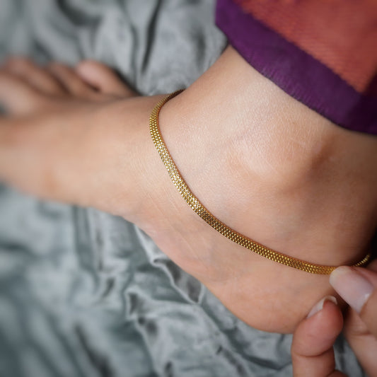 Close-up of a foot wearing a gold anklet on a grey fabric background