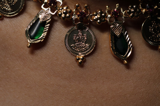 Close-up of a decorative necklace with green palakka stone and red AD with kerala traditional lekshmi idol coins and nagapadam motifs stones on a person wearing a white garment.