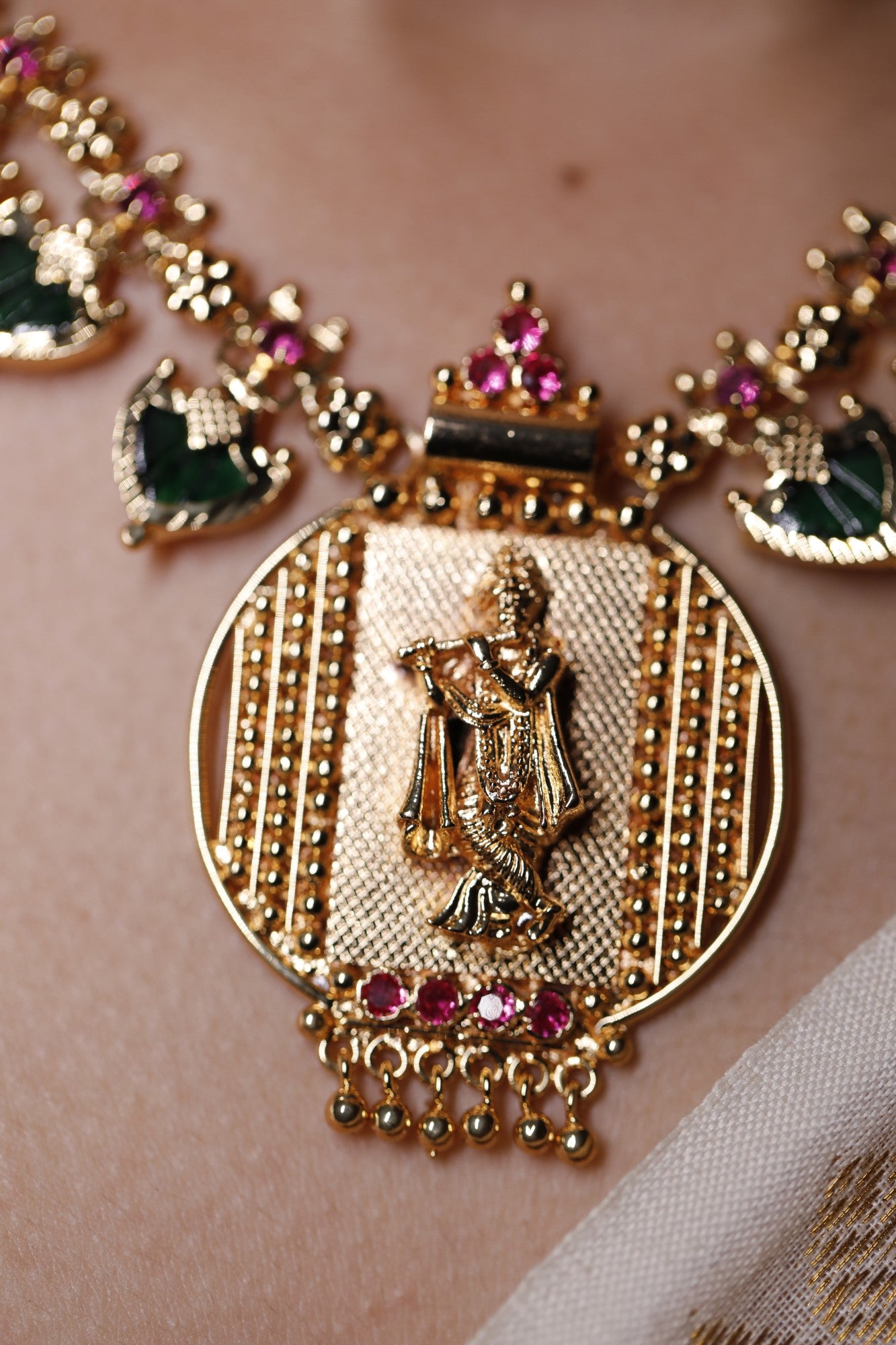 close up of Gold plated short haram type necklace with green palakka stone and red AD stones with palakka motifs worn on a neck. Krishna idol in the pendant design