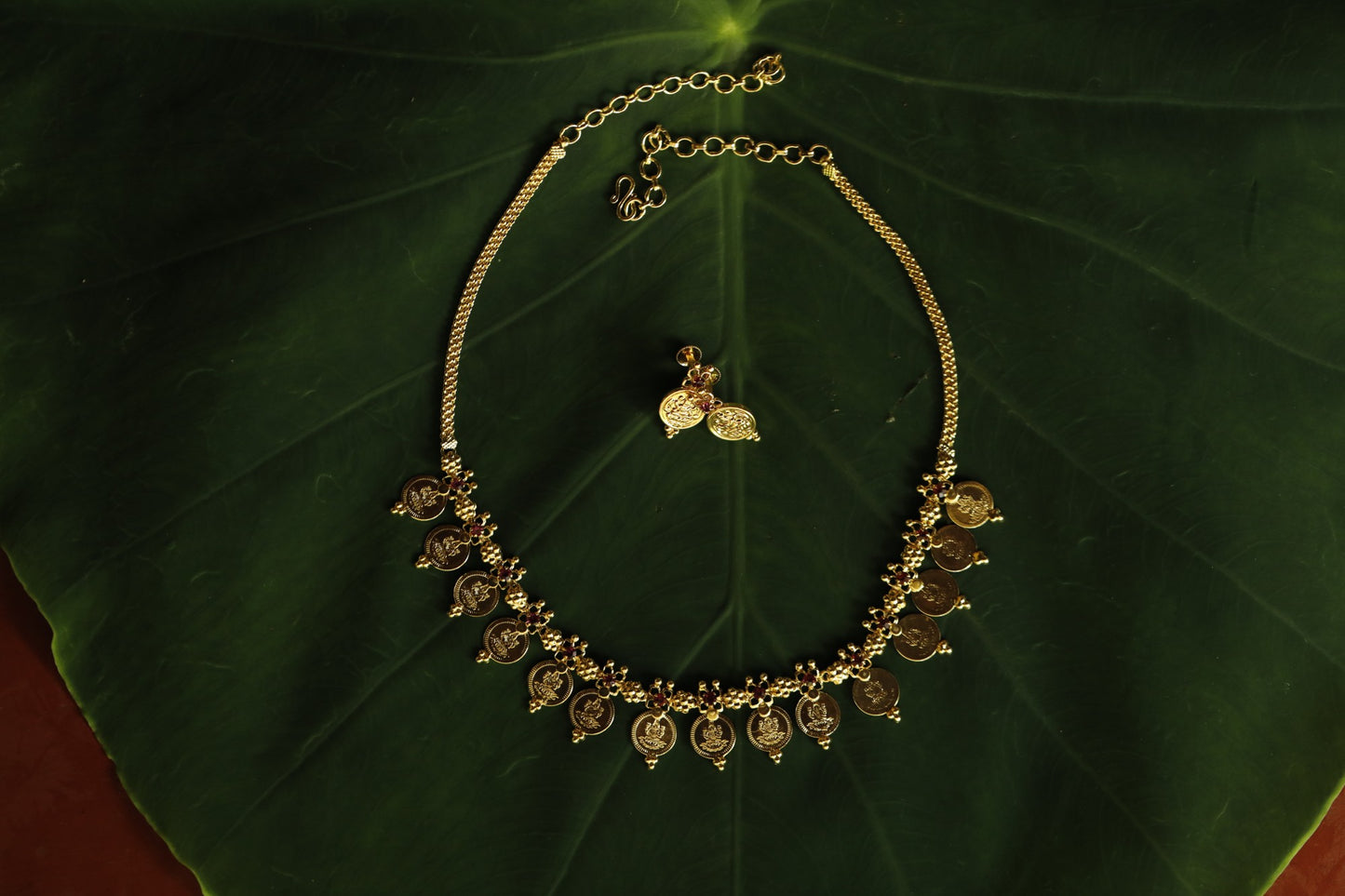 A gold alike jewellery with traditional lekshmi coin and red AD stone. This can be paired with matching lekshmi studs as in picture
