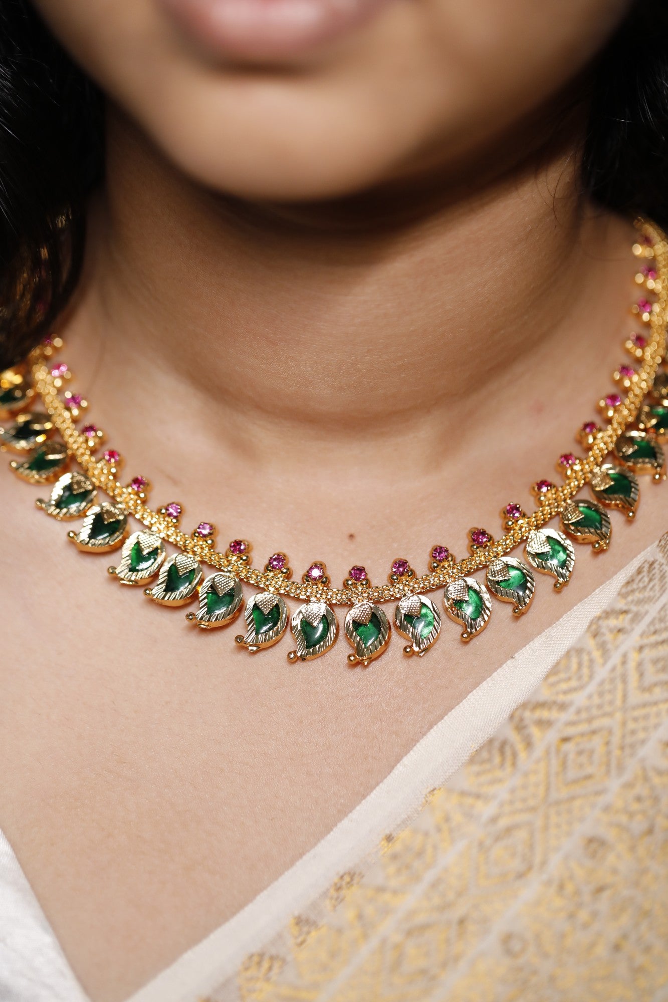 Gold plated traditional necklace with green and red and mango motifs stones worn by a person