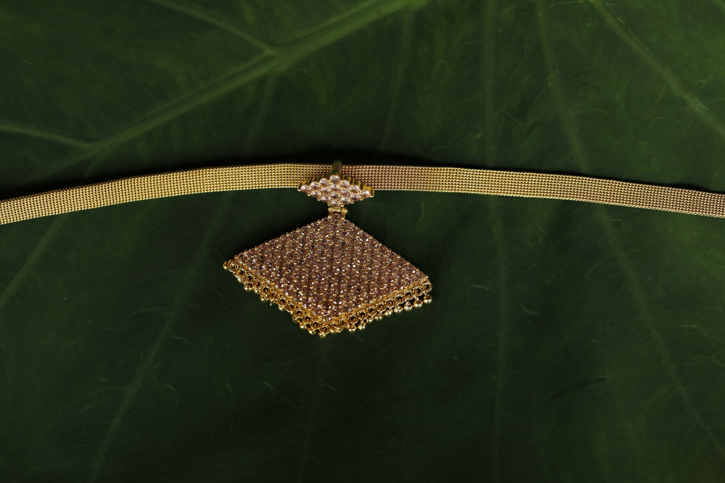 Gold necklace with a decorative pathakam pink stone pendant on a green background