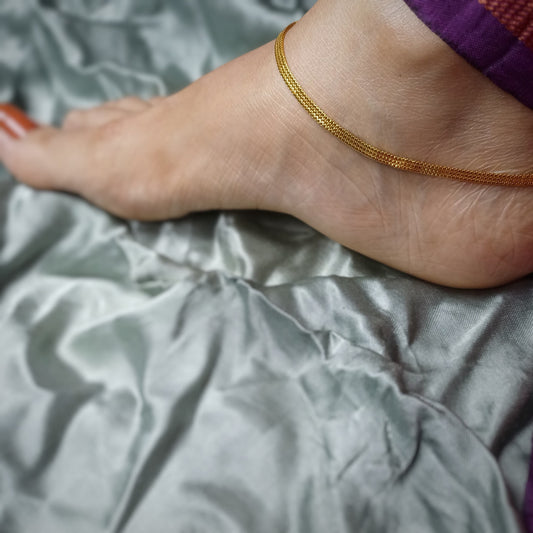 Close-up of a foot wearing a gold anklet on a gray fabric background