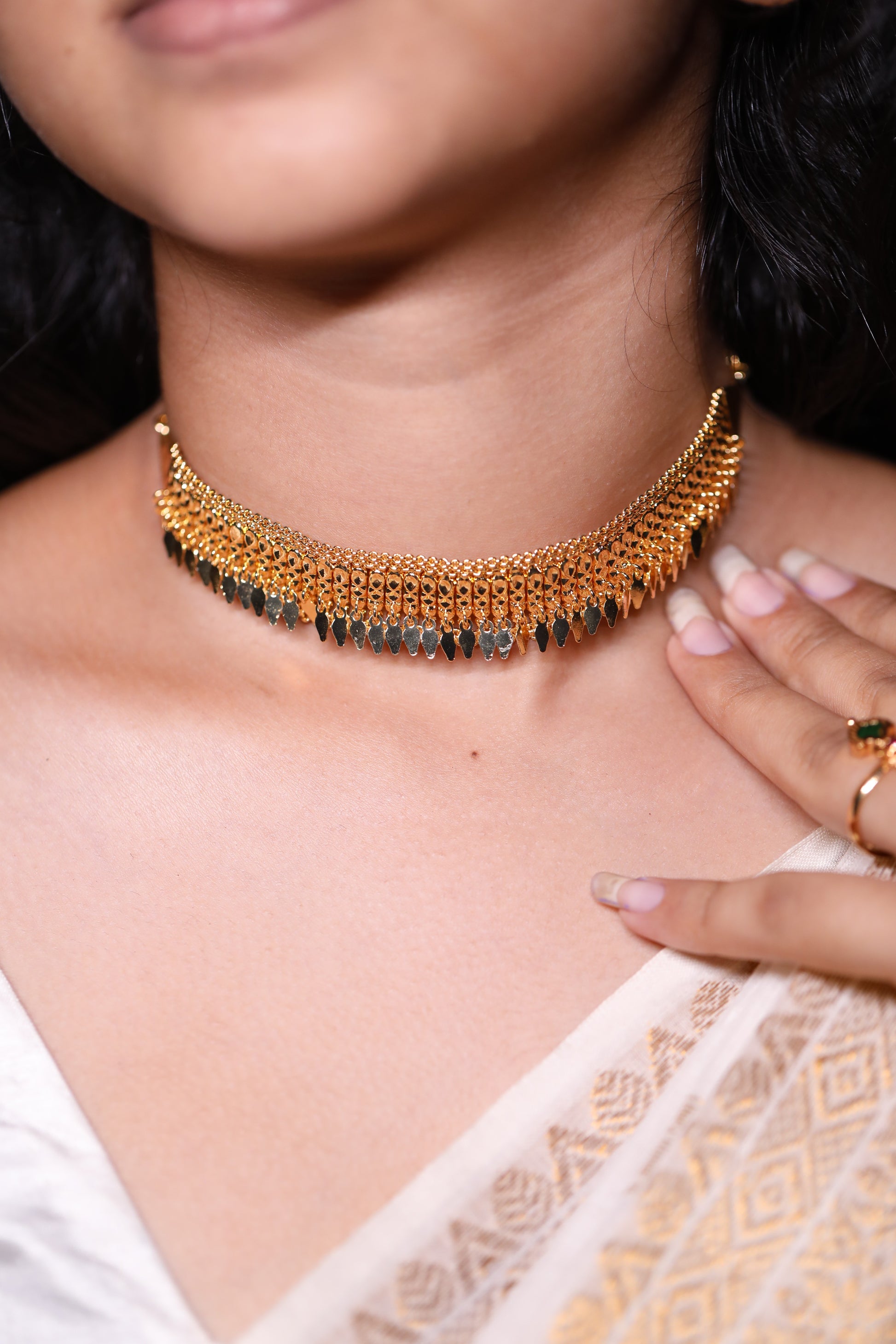 Close-up of a person wearing a traditional gold plated dangling choker type necklace with a white saree. The design is called single layer elakathali.
