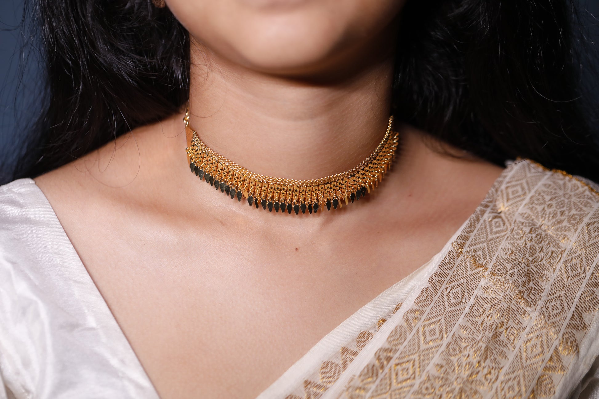 Close-up of a person wearing a traditional gold plated dangling choker type necklace with a white saree. The design is called single layer elakathali