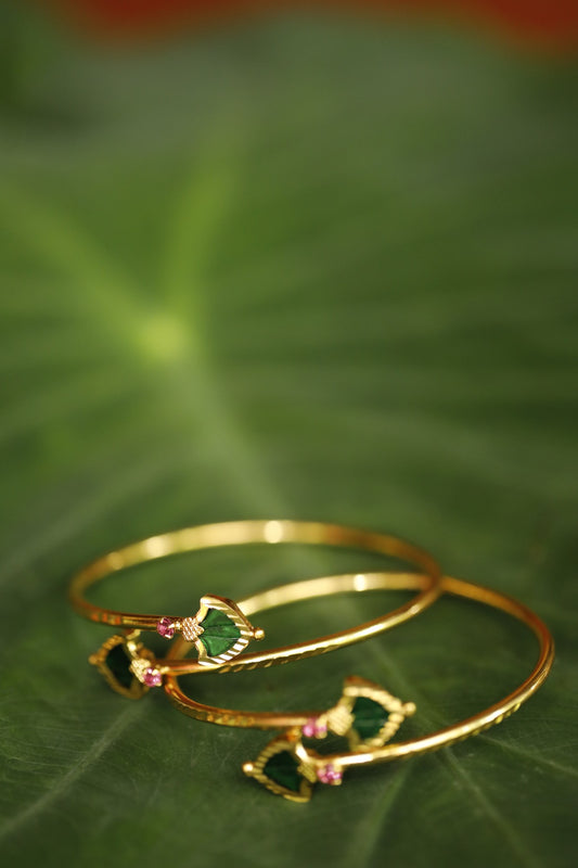 Gold plated Green Palakka stone and ruby red AD stone ajustable bangles displayed on green leafy background