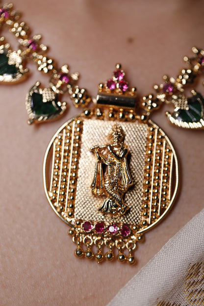 close up of Gold plated short haram type necklace with green palakka stone and red AD stones with palakka motifs worn on a neck. Krishna idol in the pendant design
