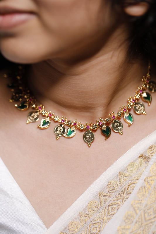 Close-up of a decorative necklace with green palakka stone and red AD with kerala traditional lekshmi idol coins and Mango motifs stones on a person wearing a white garment.