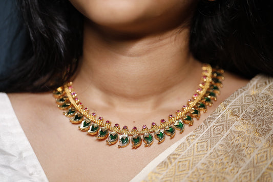 Gold plated traditional necklace with green and red and mango motifs stones worn by a person