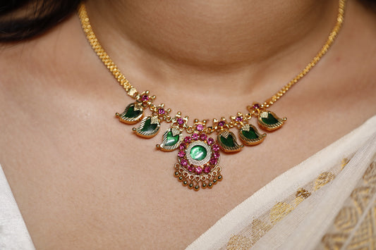 Close-up of a decorative necklace with green palakka stone and red AD stones with kerala traditional Mango motifs stones on a person wearing a white garment.