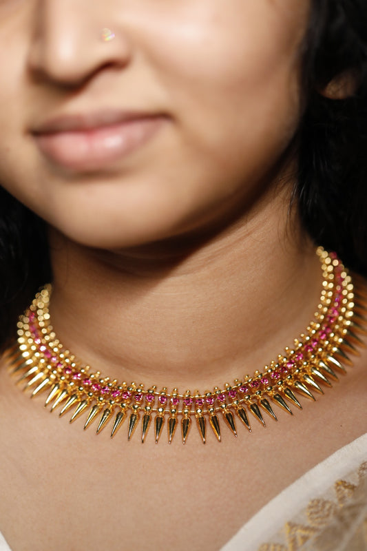 Close-up of a woman wearing aambal's mulamottu gold look alike traditional jewellery with ruby red AD stones. Mulamottu is a traditional kerala design