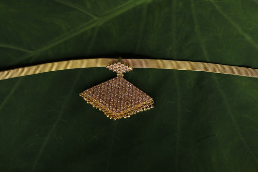 Gold necklace with a decorative pathakam pink stone pendant on a green background