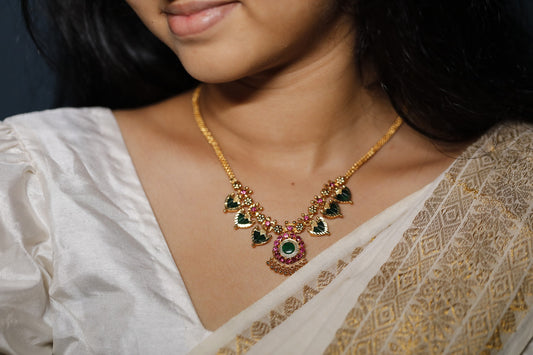 Close-up of a decorative necklace with green palakka stone and red AD stones with kerala traditional Palakka motifs on a person wearing a white saree