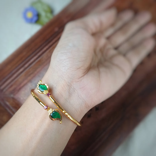 Gold look alike adjustable bangles/bracelet with green palakka gemstone on a wrist against a blurred background